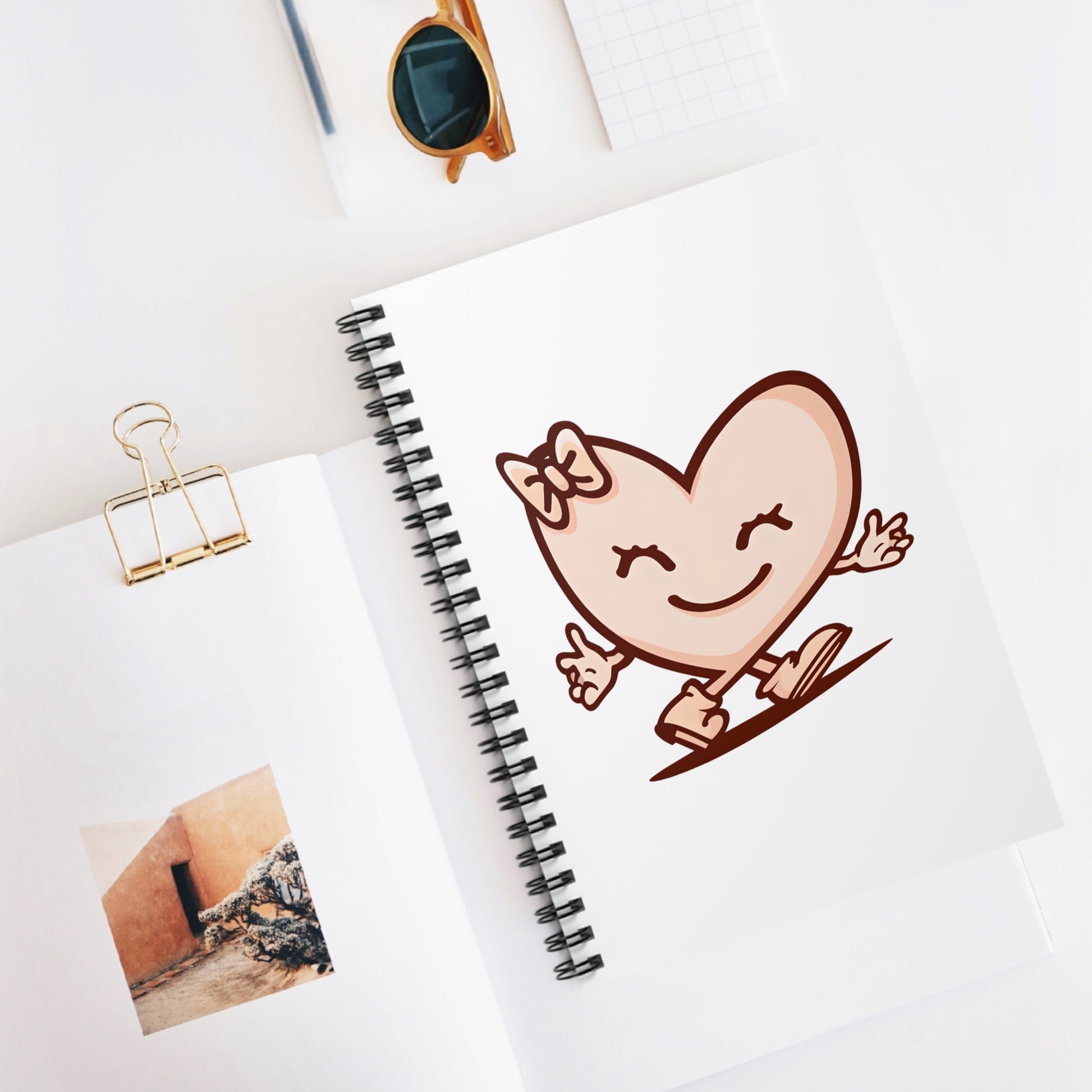 Spiral-bound notebook featuring a smiling heart character illustration, styled on a clean desk surface.
