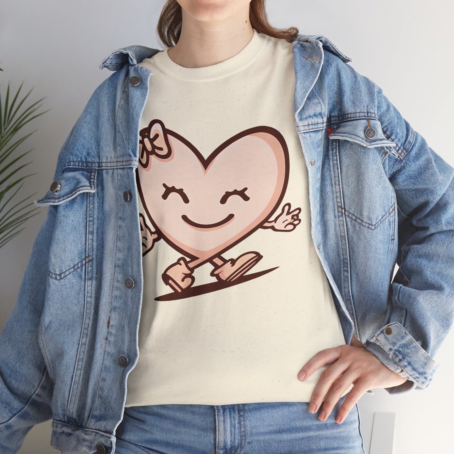 Cream graphic t-shirt featuring a smiling heart character design, styled with a light blue denim jacket in a casual lifestyle mockup.

